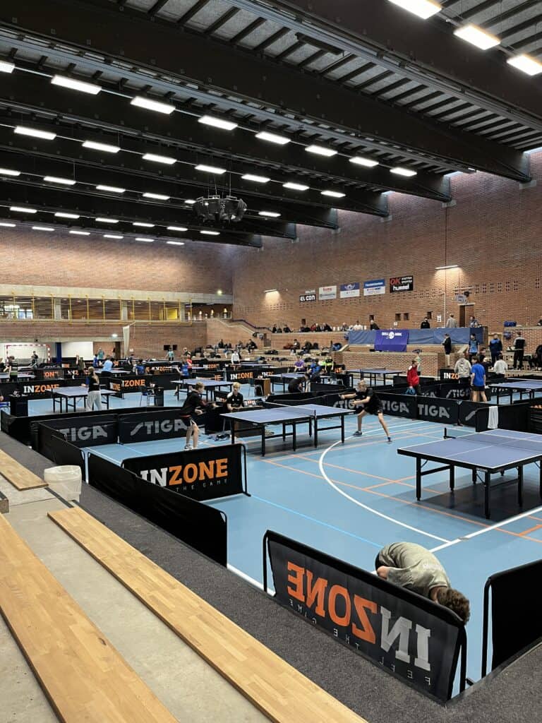 En gruppe mennesker spiller ping pong i en indendørs arena.